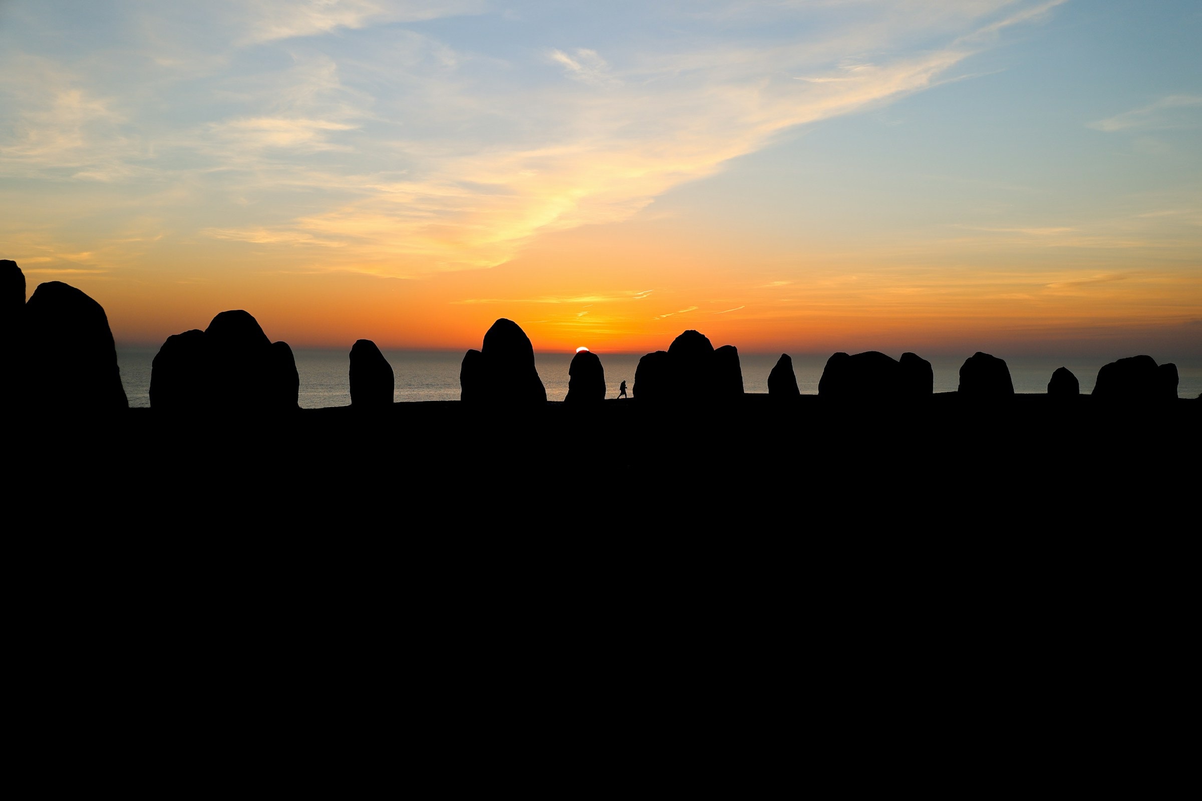 Standing stones silhouetted against a dramatic sunset sky